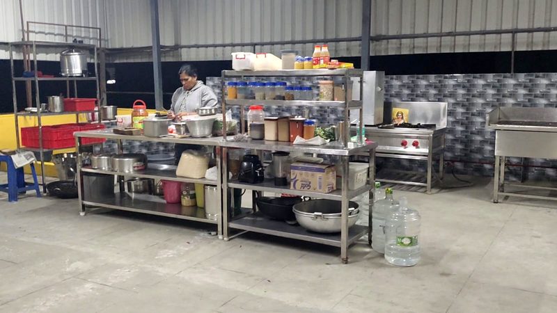 VAAV's kitchen in Perungalathur: steel prep tables, shelves of stocked spice jars, a gas range and a tiled splashback, with a cook preparing an order.